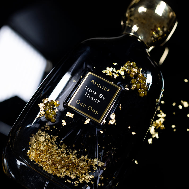 Noir By Night Atelier Des Ors perfume bottle with black glass and gold accents on dark background