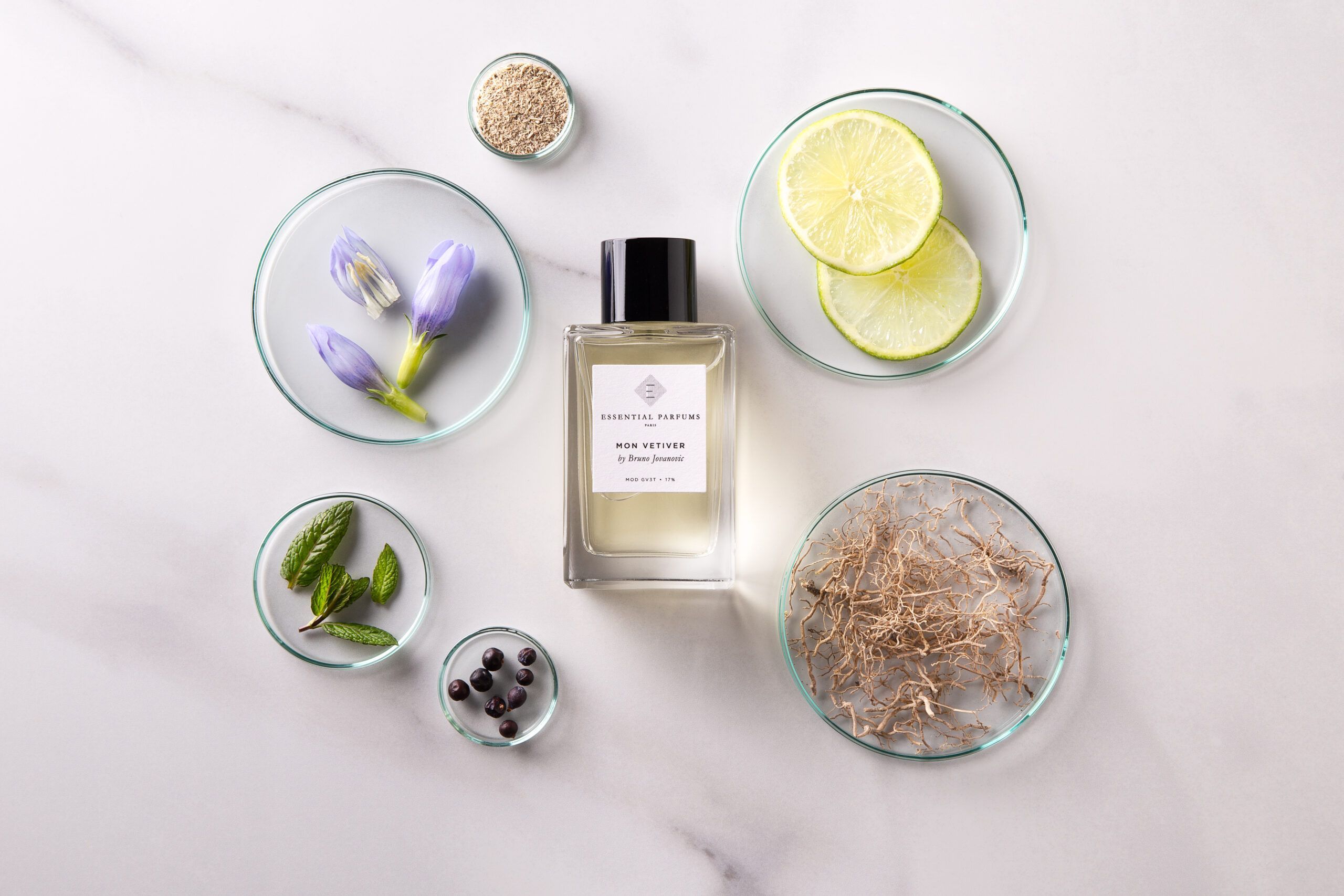 Essential Parfums Mon Vetiver 100ml perfume bottle with natural ingredients like lime, mint, and flowers on marble surface