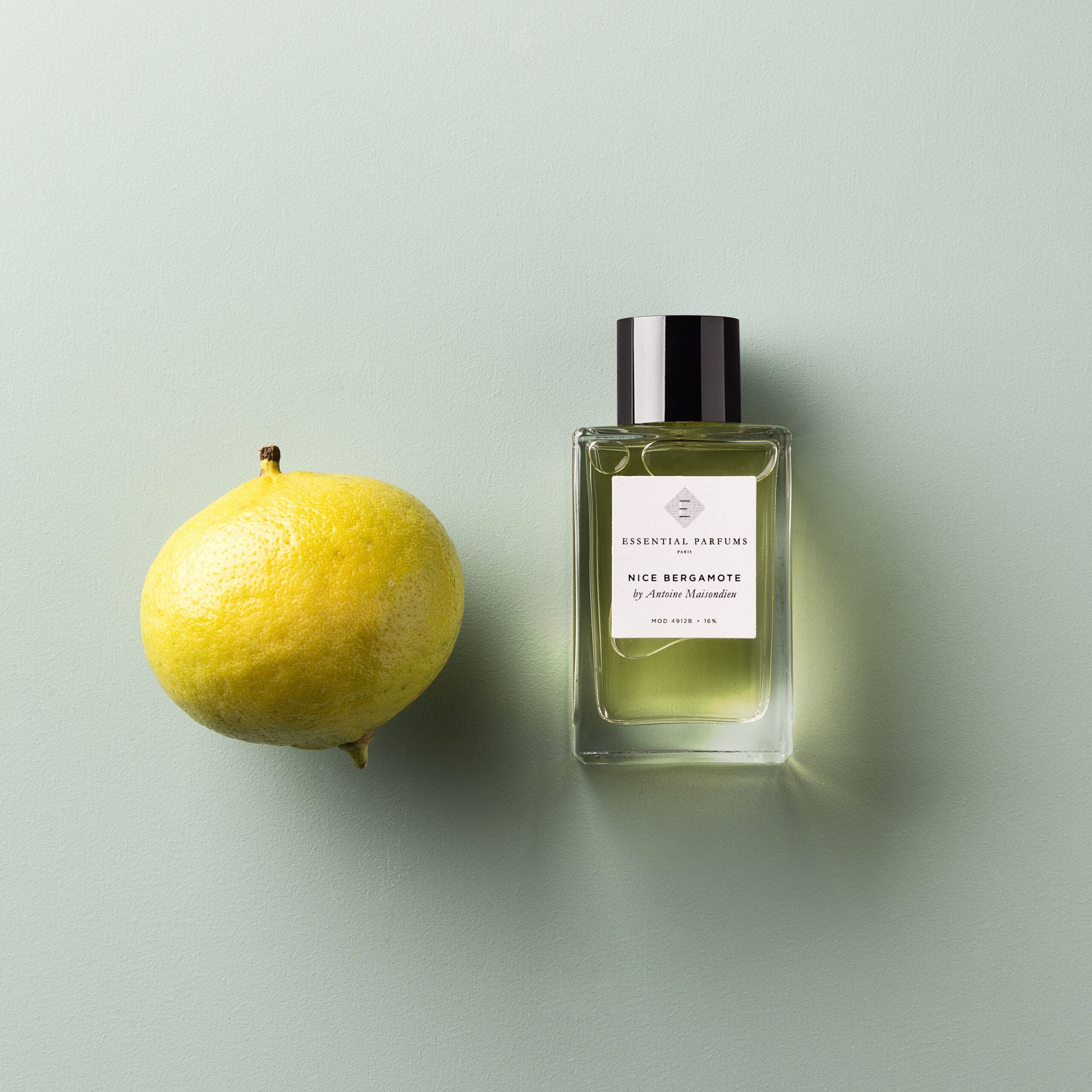 Essential Parfums Nice Bergamote perfume bottle next to fresh bergamot fruit on light green background