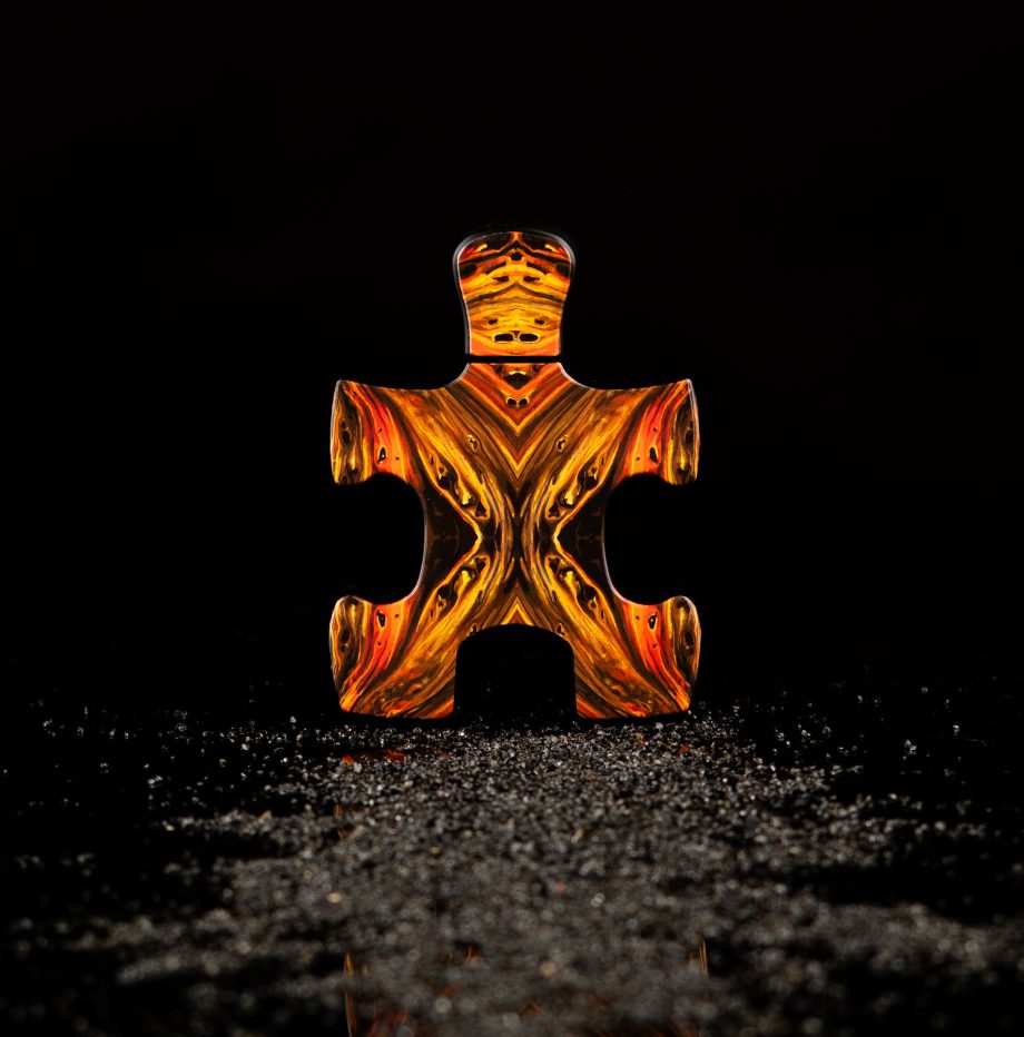 Puzzle Lal fragrance perfume bottle shaped like a fiery orange puzzle piece against a dark background