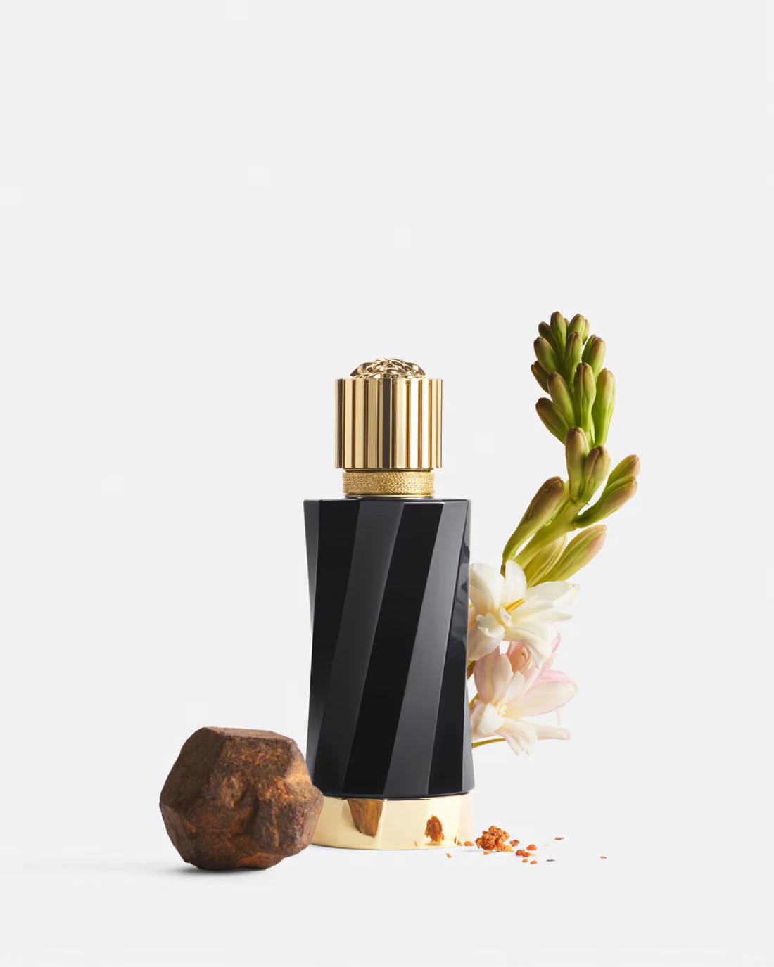 Versace Atelier Reve de Myrrhe perfume bottle with gold cap next to flowers and resin on white background