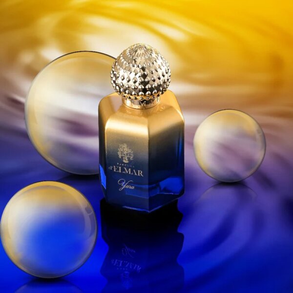 DELMAR YARA perfume for women in a blue and gold bottle with decorative cap on reflective surface