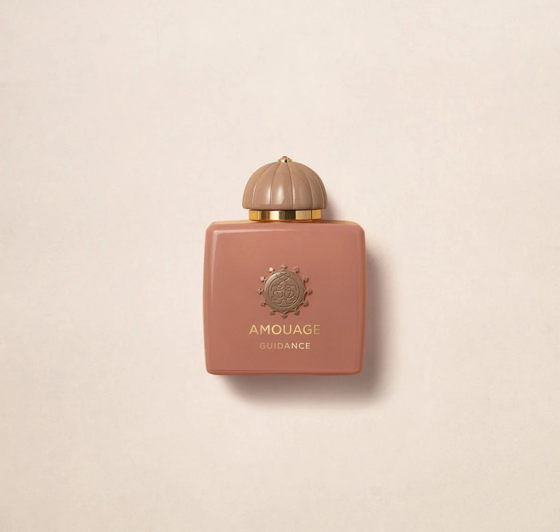 Amouage Guidance perfume bottle with a matte pink finish and gold detailing on a beige background