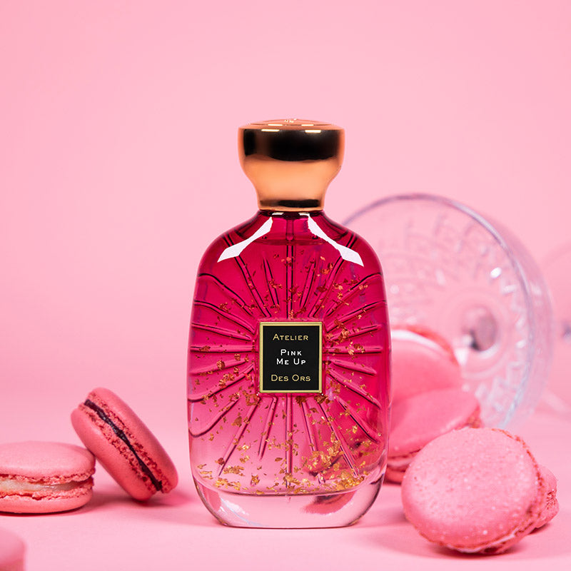 Atelier Des Ors Pink Me Up perfume bottle with gold details surrounded by pink macarons on pink background