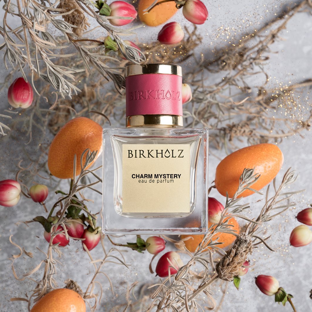 Birkholz Charm Mystery eau de parfum bottle surrounded by dried flowers and orange fruits on gray background