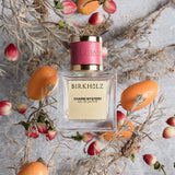 Birkholz Charm Mystery eau de parfum bottle surrounded by dried flowers and orange fruits on gray background