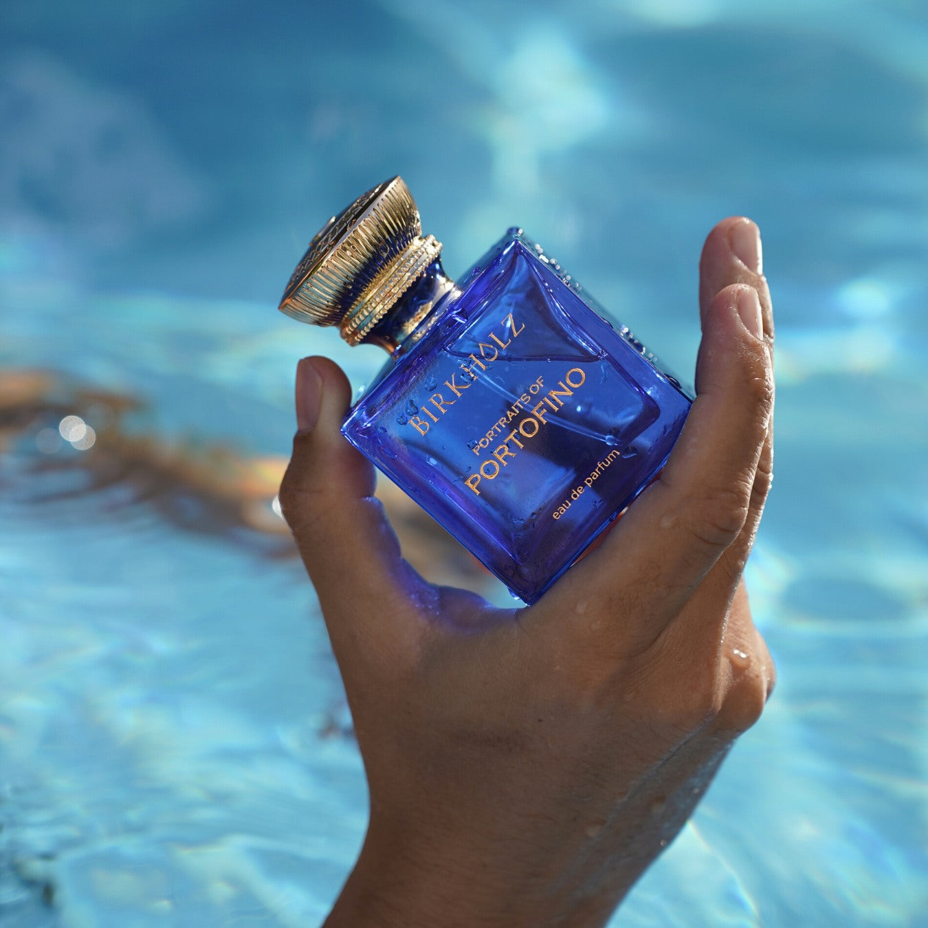 Hand holding Birkholz Portraits of Portofino perfume bottle with blue ocean water background