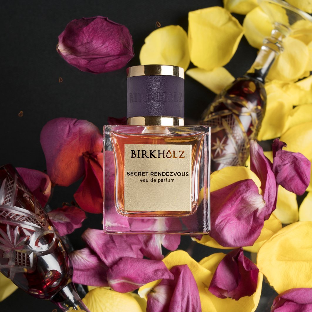 Birkholz Secret Rendezvous Eau de Parfum bottle surrounded by purple and yellow rose petals
