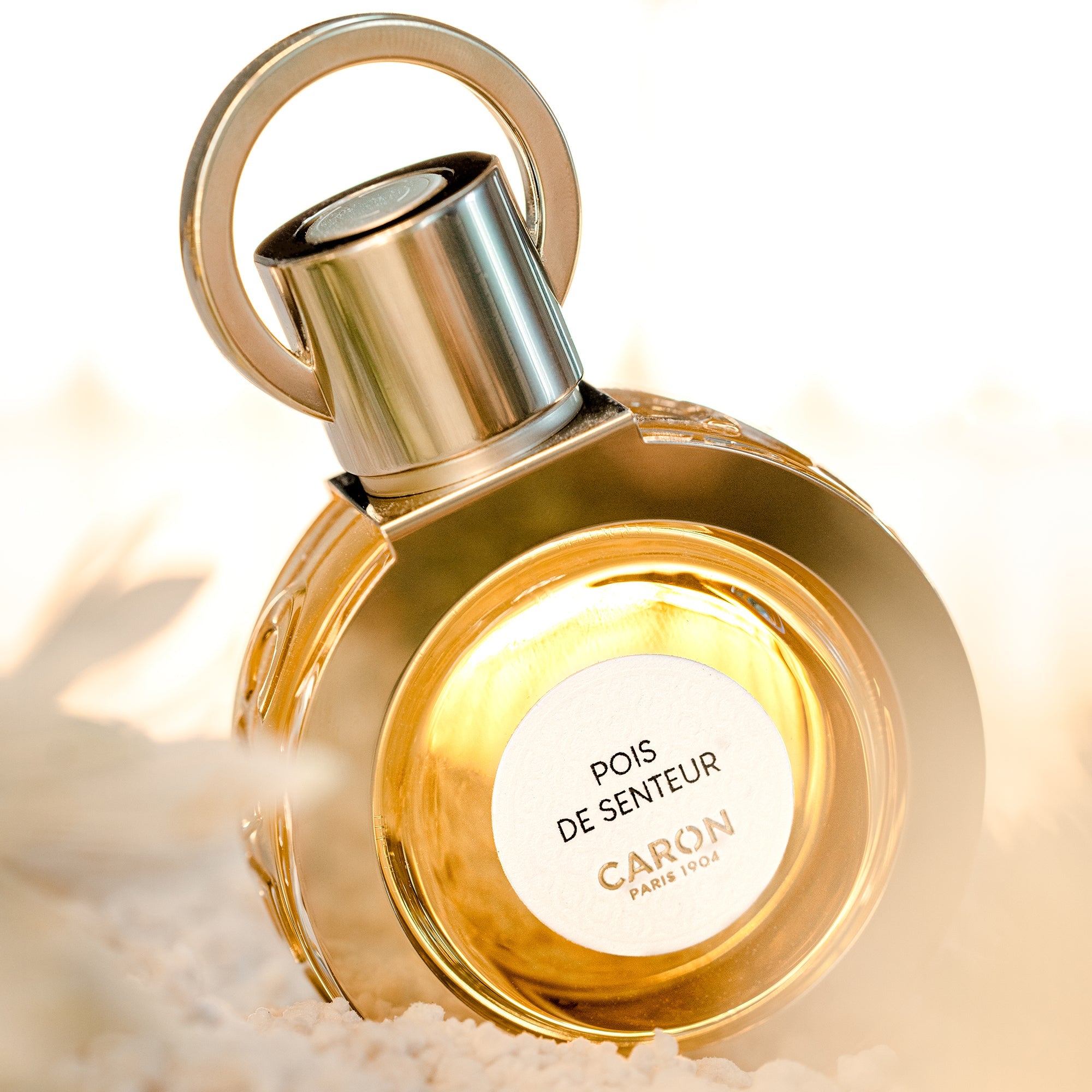 Caron Pois De Senteur Extrait de Parfum in a round golden bottle with metallic cap on soft background