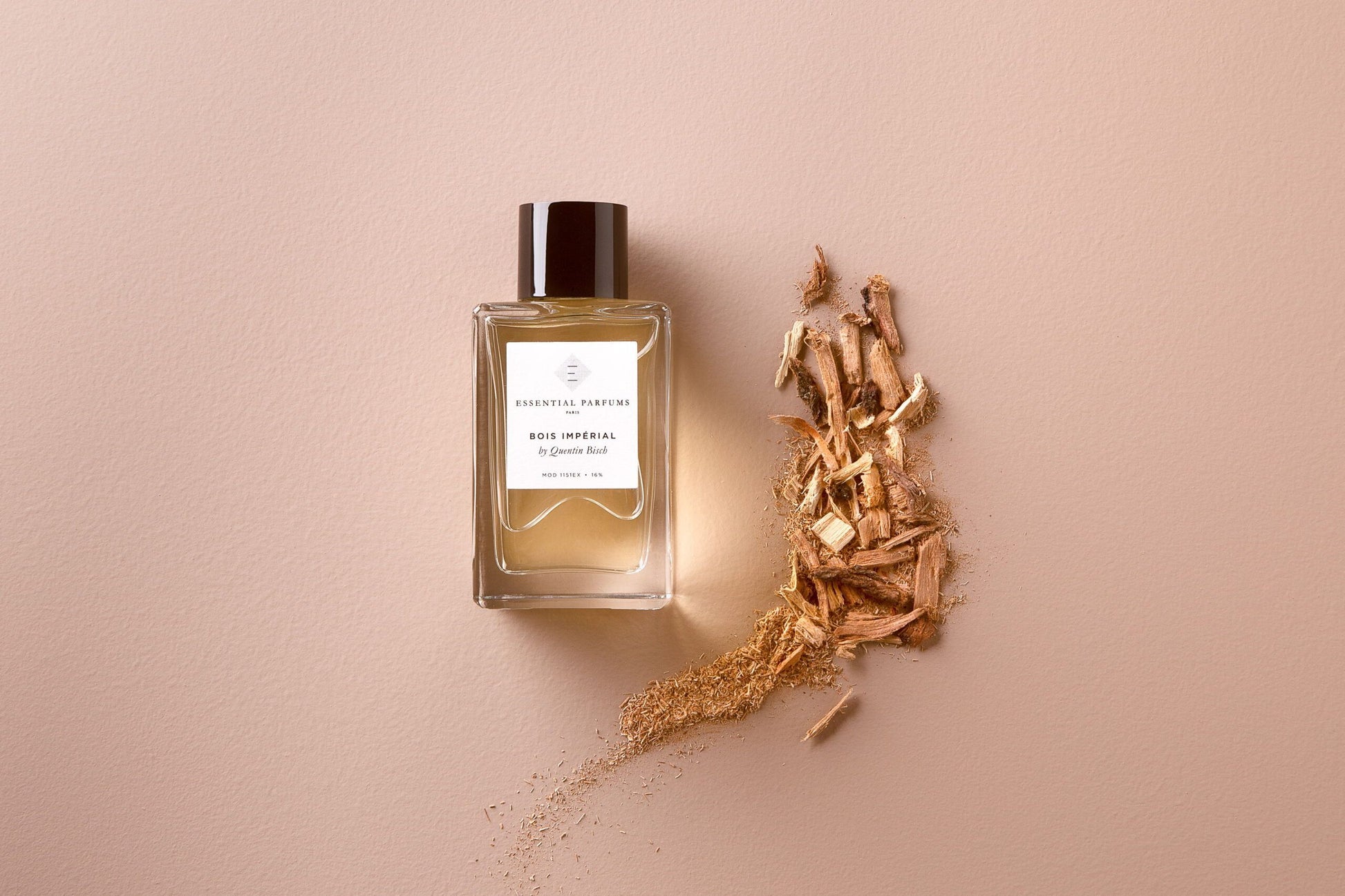 Essential Parfums Bois Imperial Eau de Parfum bottle next to wood chips on beige background