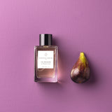 Essential Parfums Fig Infusion perfume bottle next to a fresh fig on a purple background