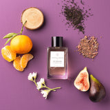 Essential Parfums Fig Infusion perfume bottle surrounded by fig, tangerine, flowers, and natural ingredients on purple background