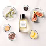 Essential Parfums Fig Infusion perfume bottle surrounded by fresh figs, flowers, citrus, spices, and wood elements