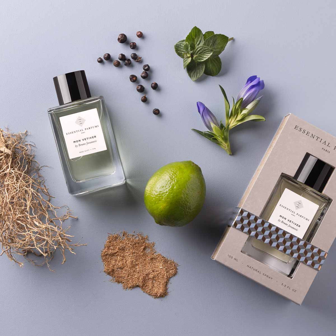 Essential Parfums Mon Vetiver 100ml perfume bottle with packaging and natural ingredients on a gray surface