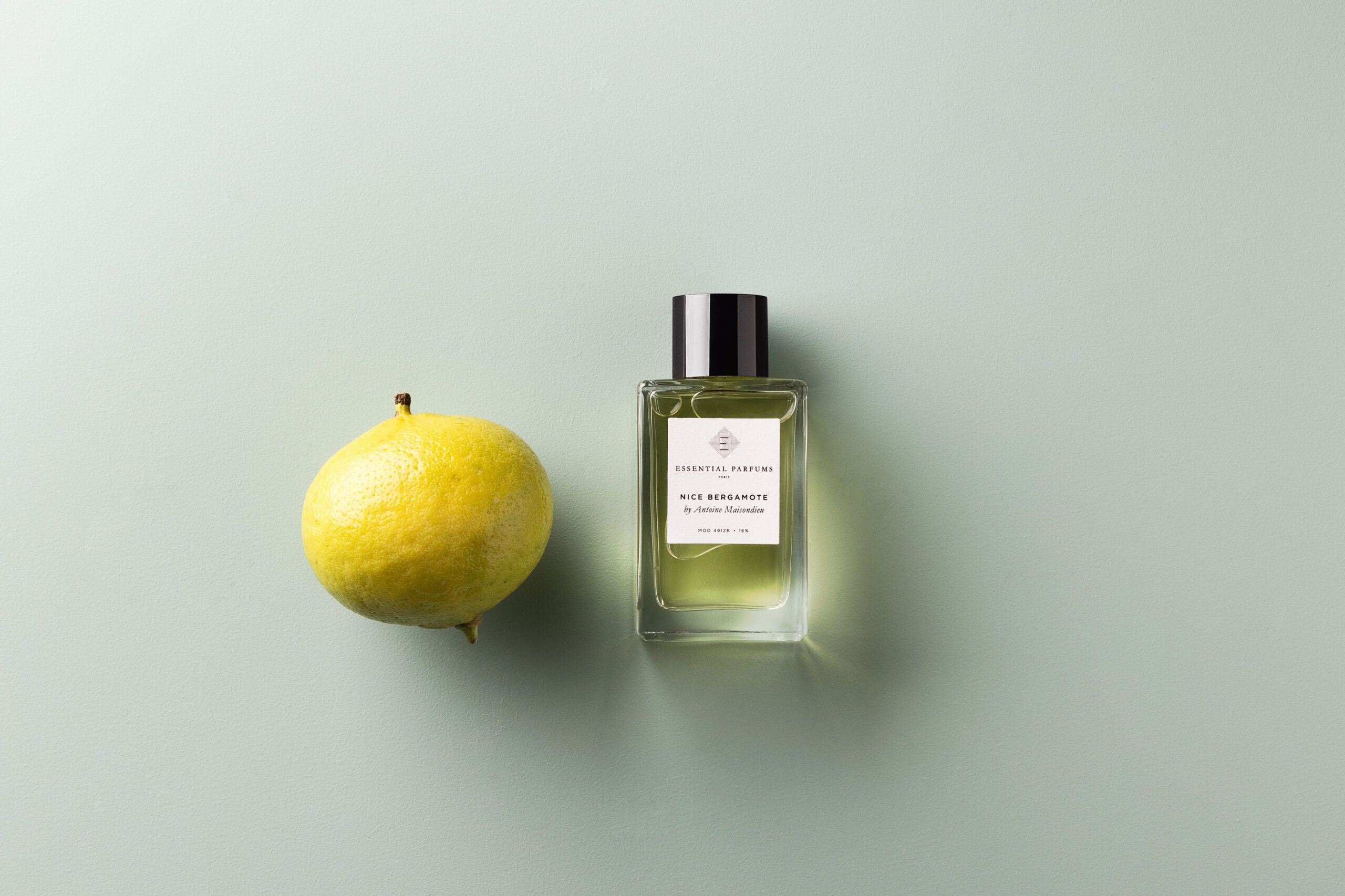Essential Parfums Nice Bergamote perfume bottle next to a fresh bergamot fruit on light background