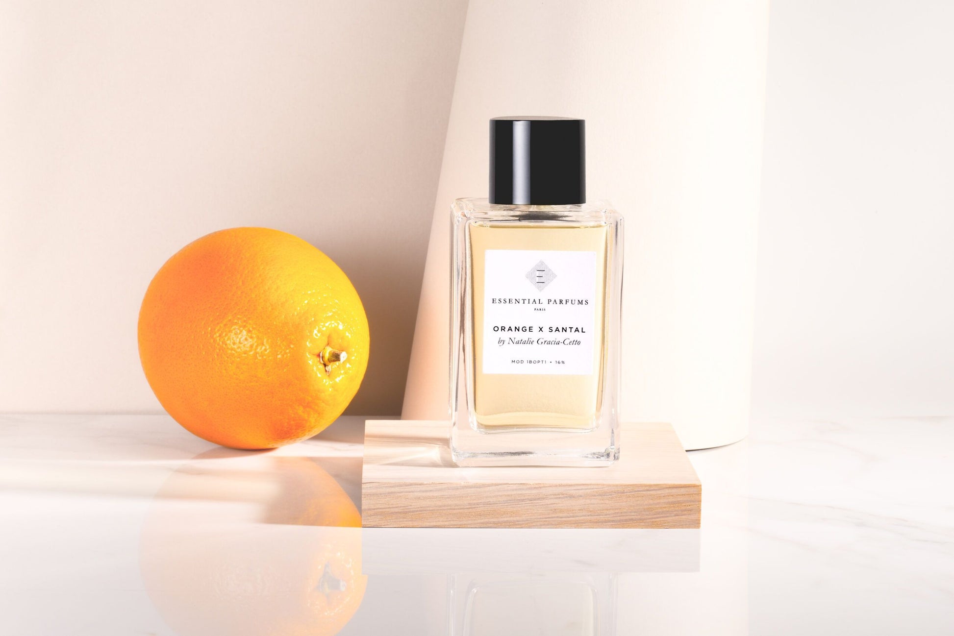 Essential Parfums Orange X Santal 100ml perfume bottle displayed with a fresh orange on a wooden platform