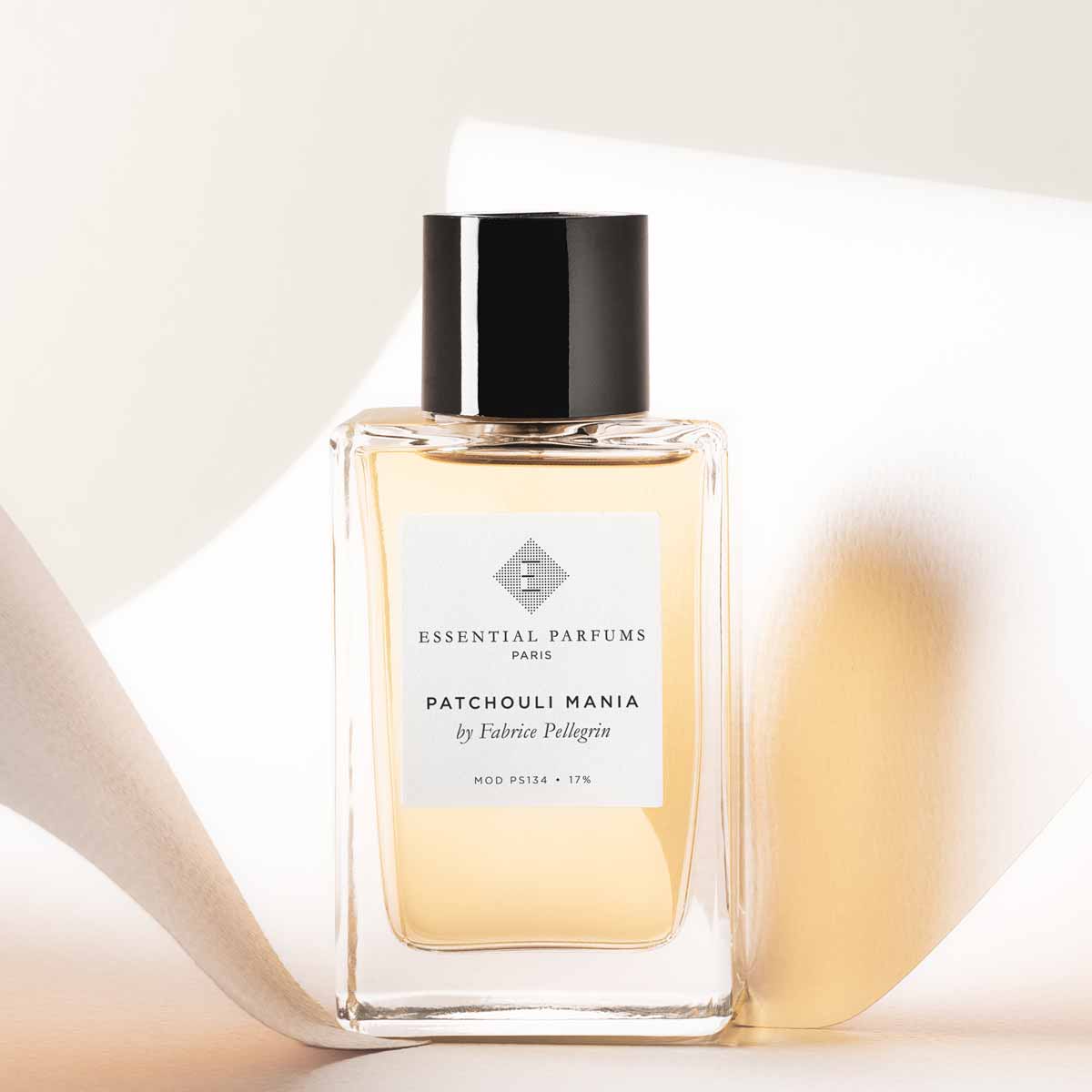 Essential Parfums Patchouli Mania perfume bottle with clear glass and black cap on neutral background