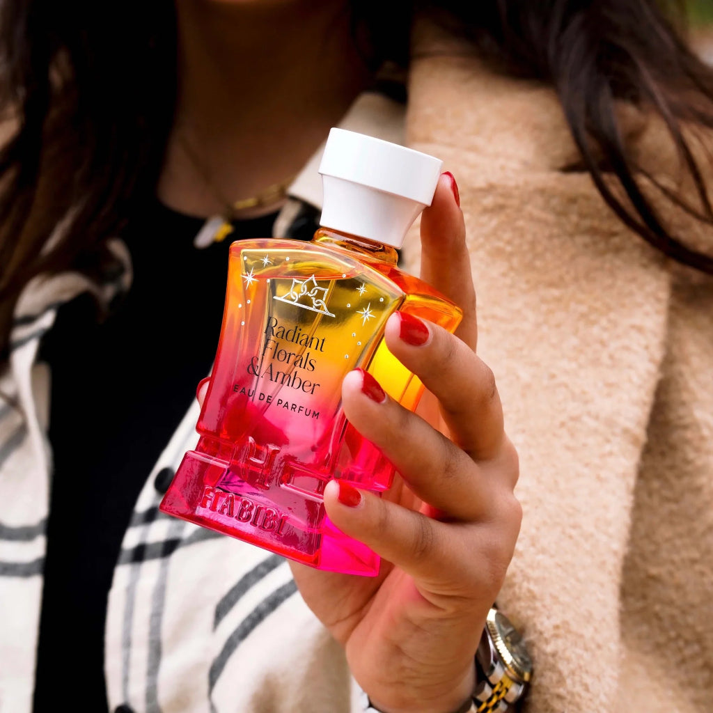 Radiant Florals & Amber perfume by HABIBI NEW YORK held in hand with multicolor pink and orange bottle
