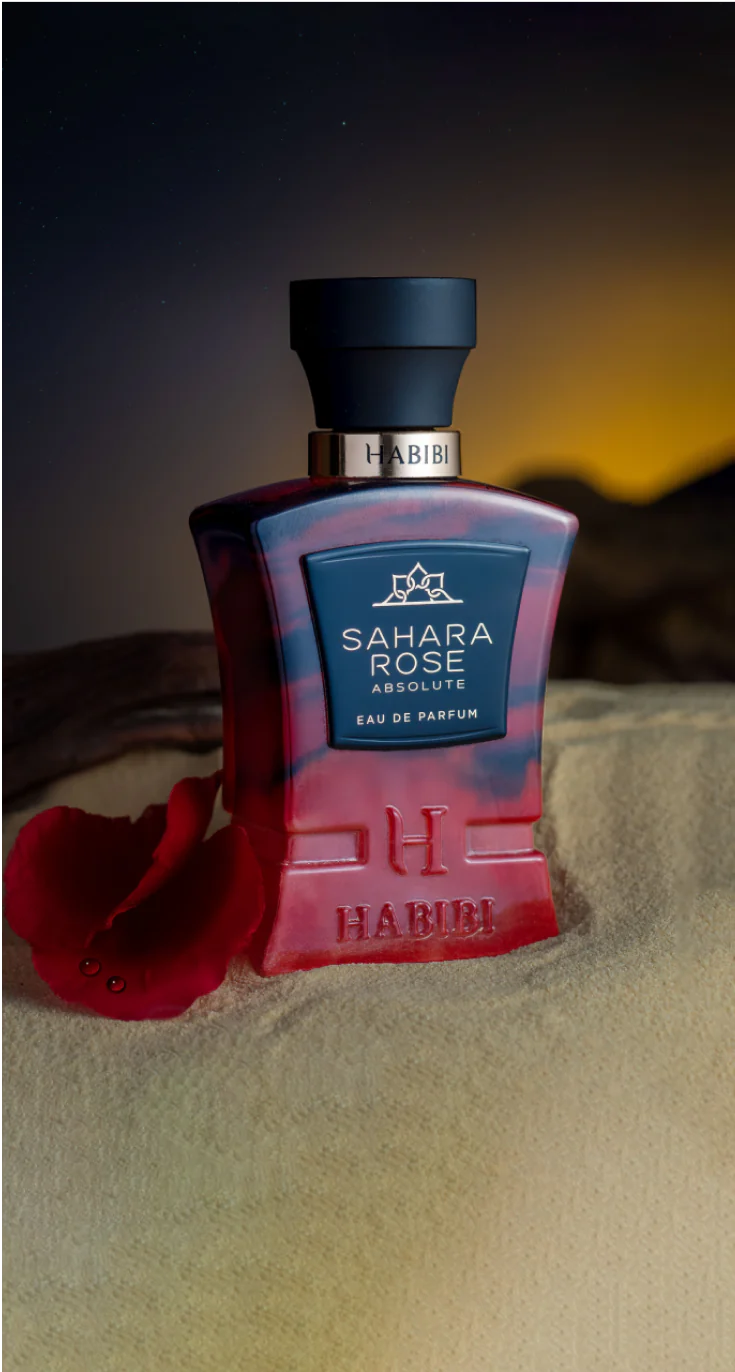 HABIBI NEW YORK Sahara Rose Absolute perfume bottle with deep red and blue hues on sandy surface