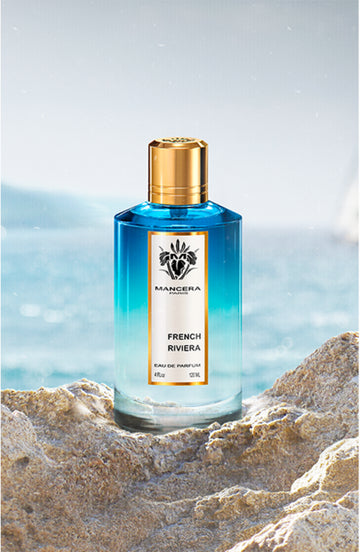 Mancera French Riviera Eau de Parfum bottle with blue gradient glass and gold cap on rocky beach background