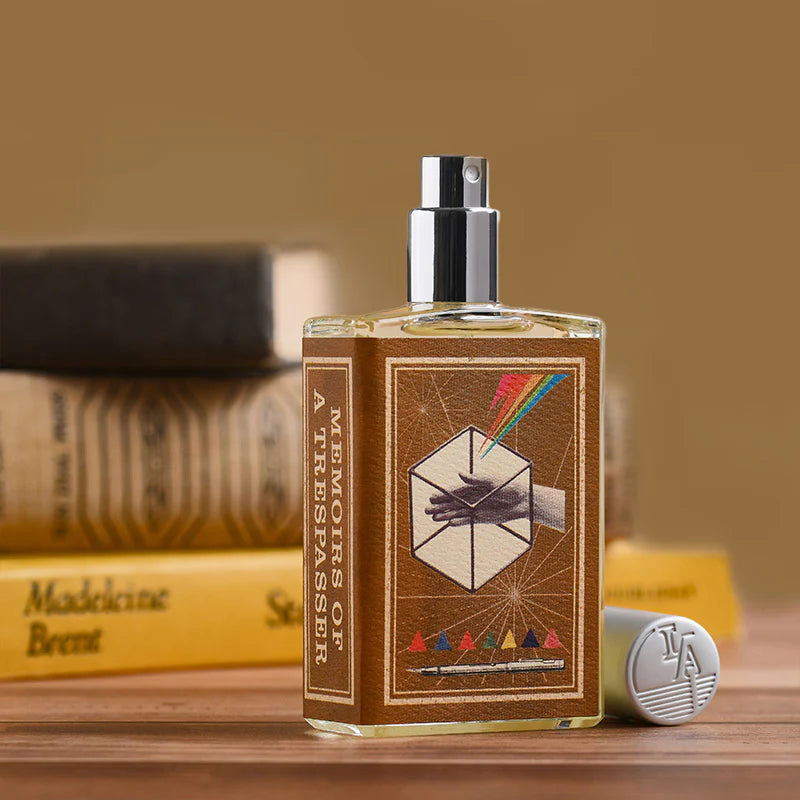 Imaginary Authors MEMOIRS OF A TRESPASSER fragrance bottle with brown label and colorful design on wooden surface