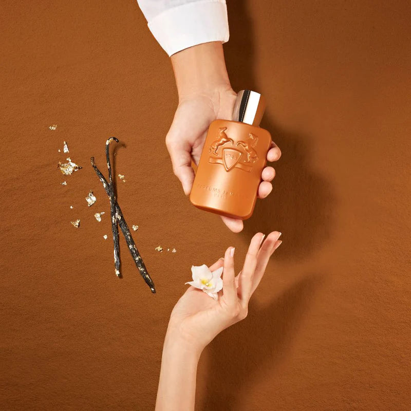 Parfums de Marly Althair EDP 125ml held above hand with vanilla pods and flower on brown background