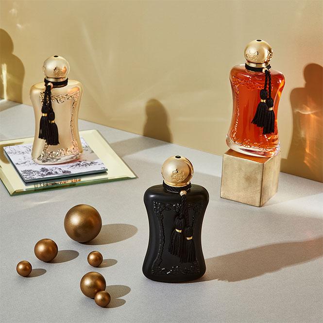 Parfums De Marly Darcy EDP 75ml perfume bottles in gold, amber, and black with decorative tassels on a neutral background