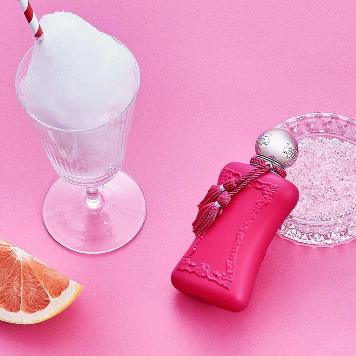 Parfums De Marly Oriana 75ml pink perfume bottle with tassel next to grapefruit slice and iced drink on pink background
