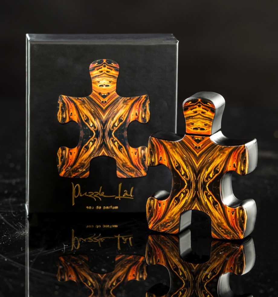Puzzle Lal fragrance perfume bottle shaped like a puzzle piece with black and orange design beside matching box