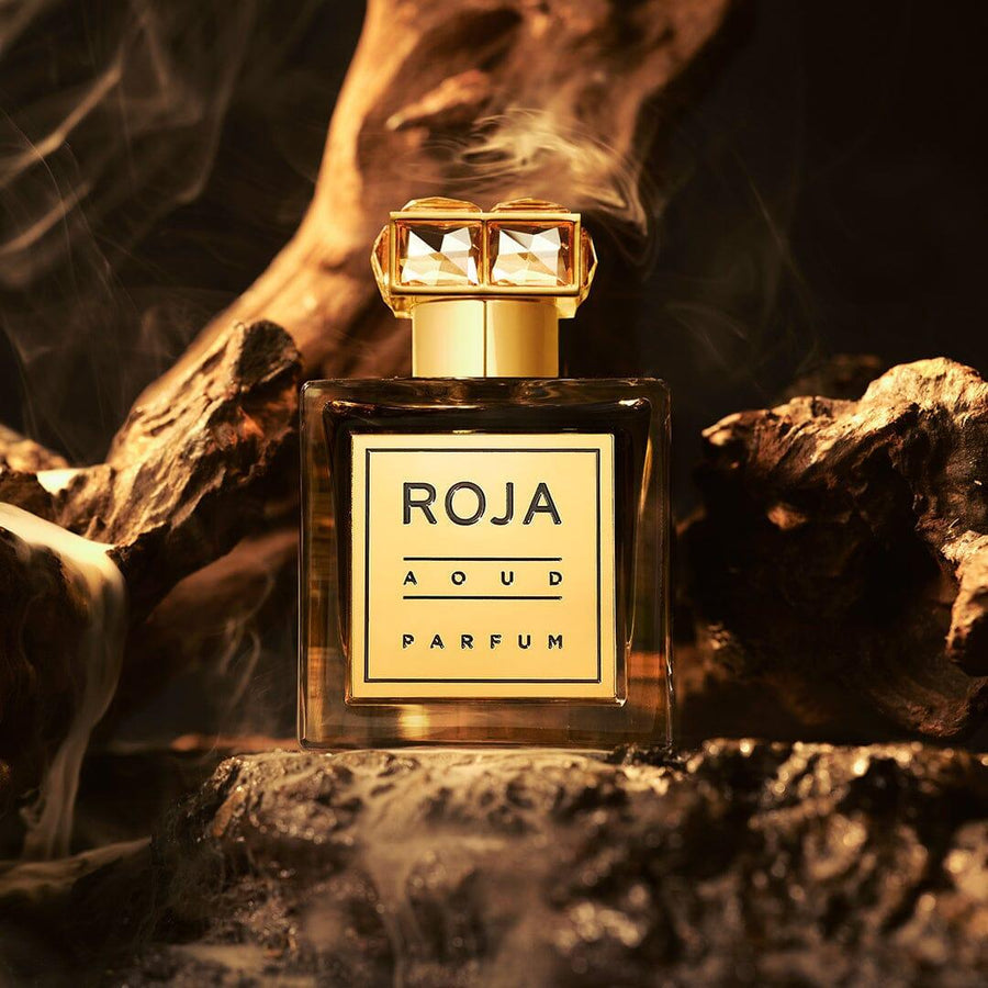 Roja Parfums Aoud Crystal perfume bottle with gold accents set against smoky dark wood background