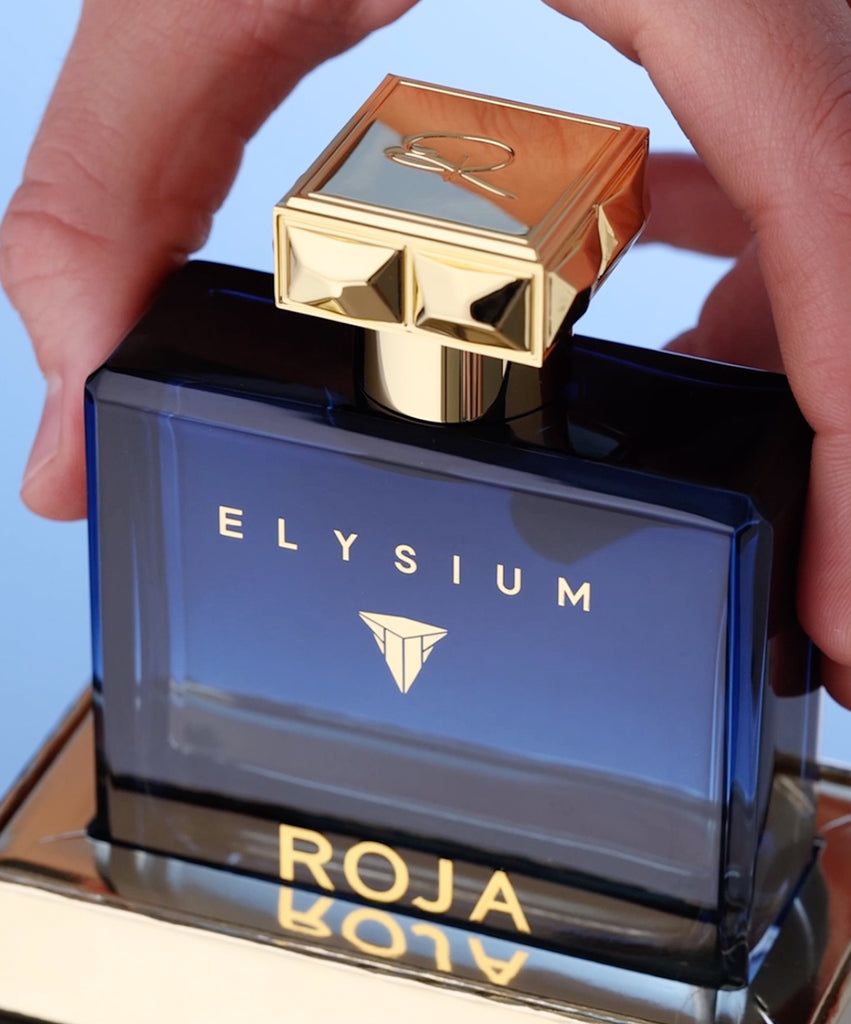 Roja Parfums Elysium perfume for men in blue bottle with gold cap held by hand