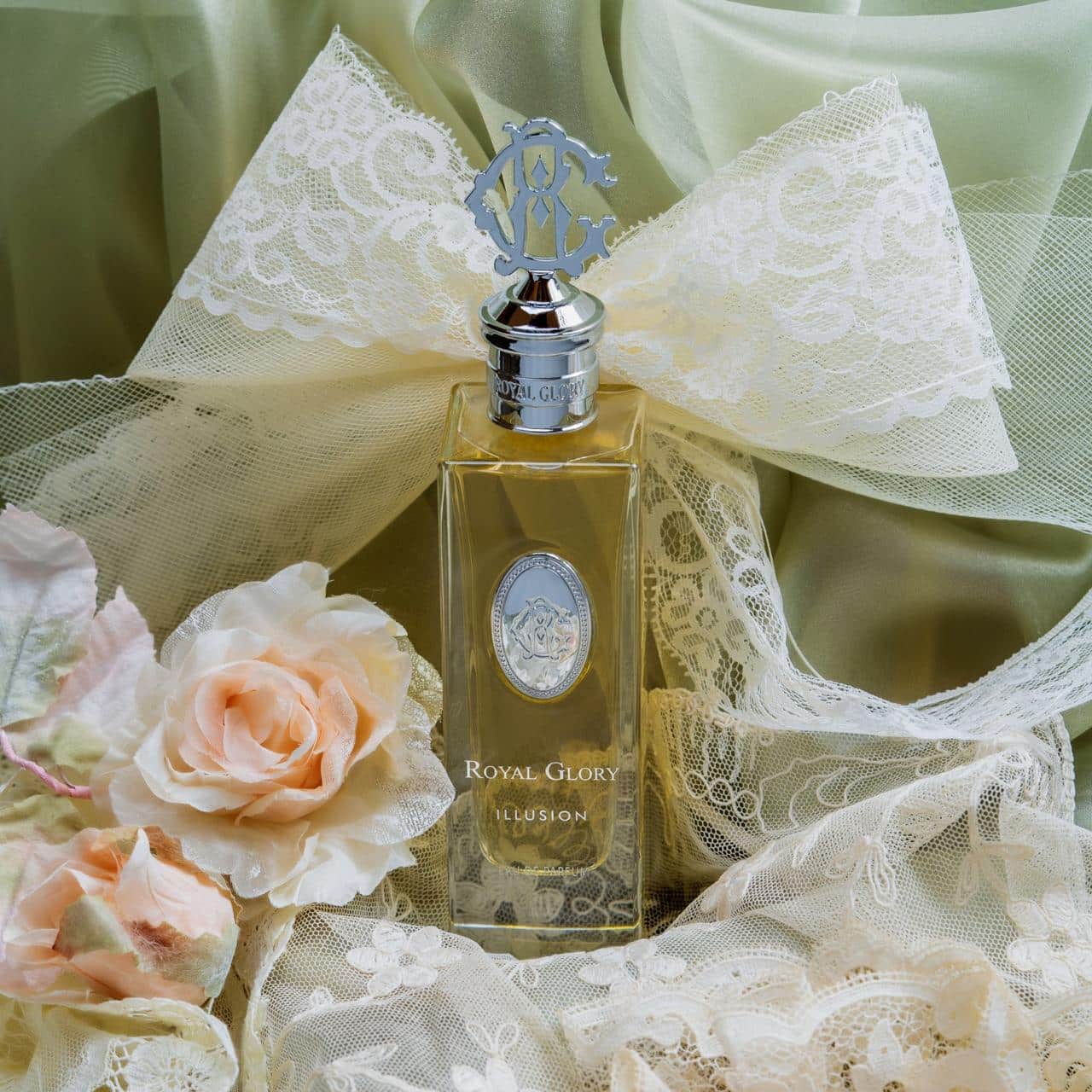 Royal Glory Illusion Eau de Parfum bottle with silver cap and lace bow surrounded by soft peach roses