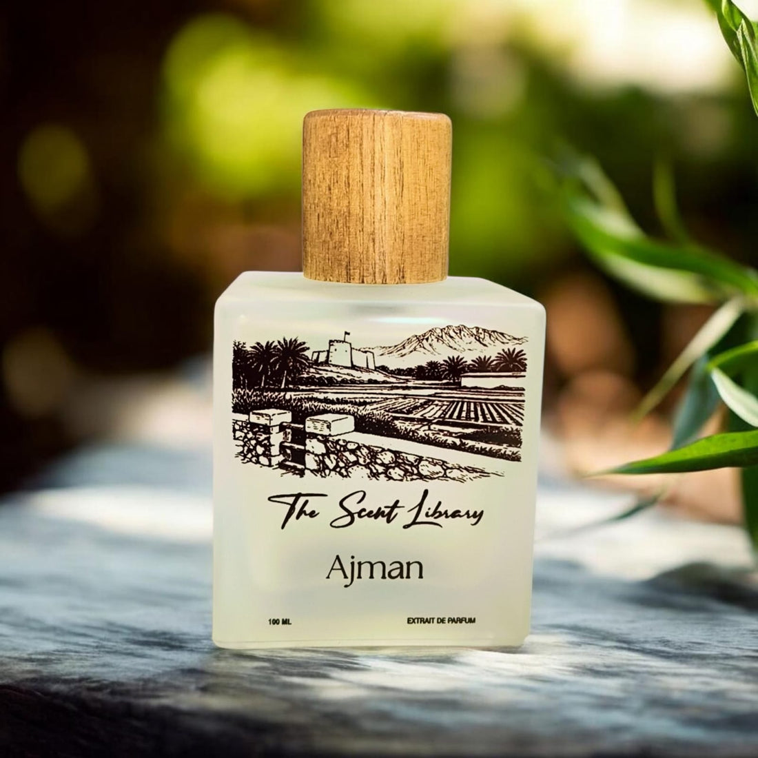 Ajman extrait de parfum by The Scent Library, a frosted glass bottle with a wooden cap and an illustrated label of a fort, palm farm and mountains