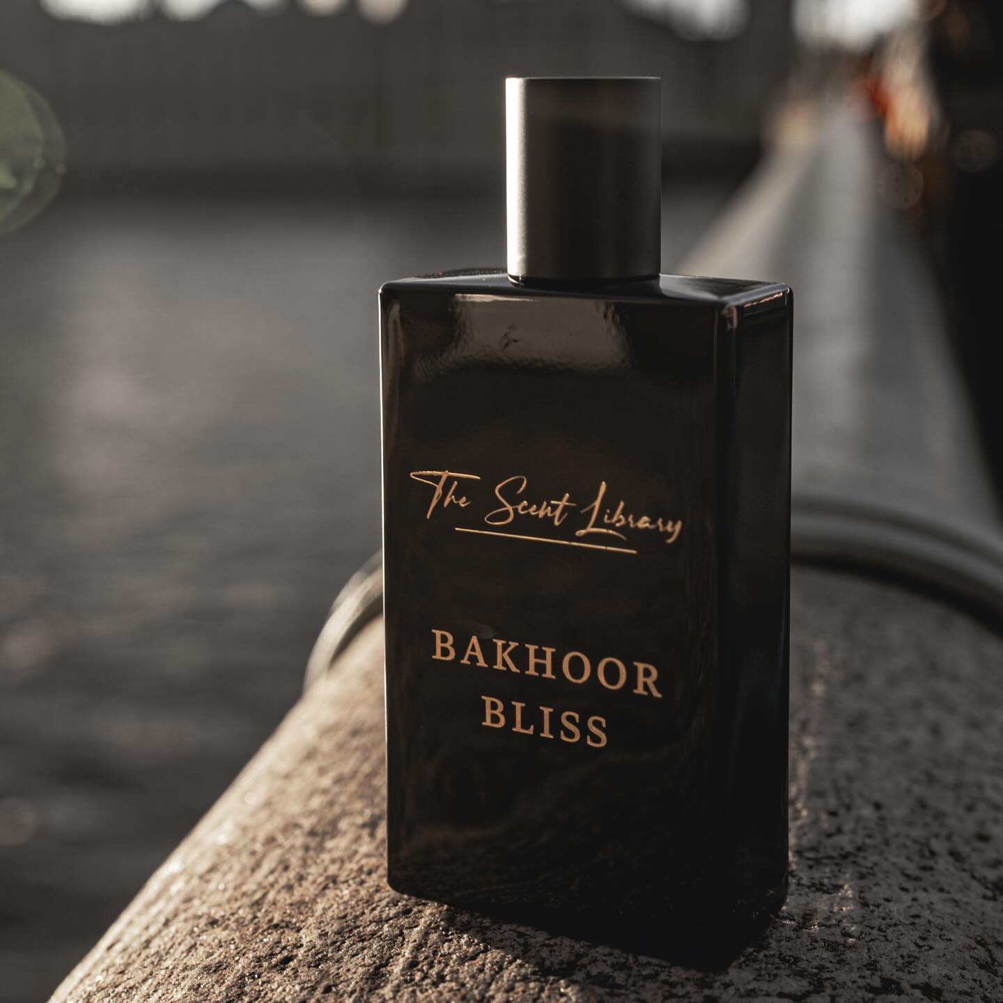 The Scent Library Bakhoor Bliss fragrance bottle displayed on a stone ledge near water