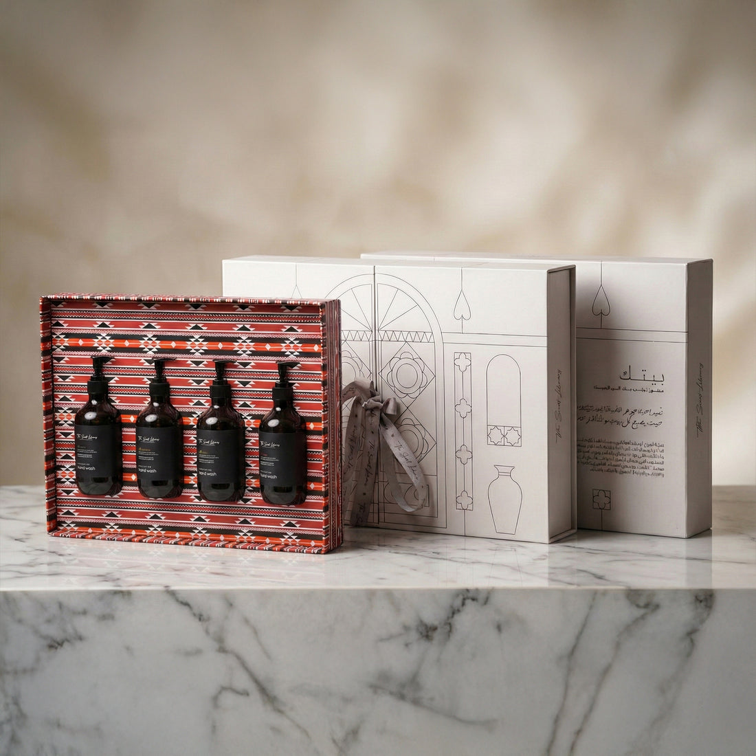 The Residence Collection by Baytak, four amber hand wash bottles in a red Sadu-patterned gift box beside a white presentation box, by The Scent Library