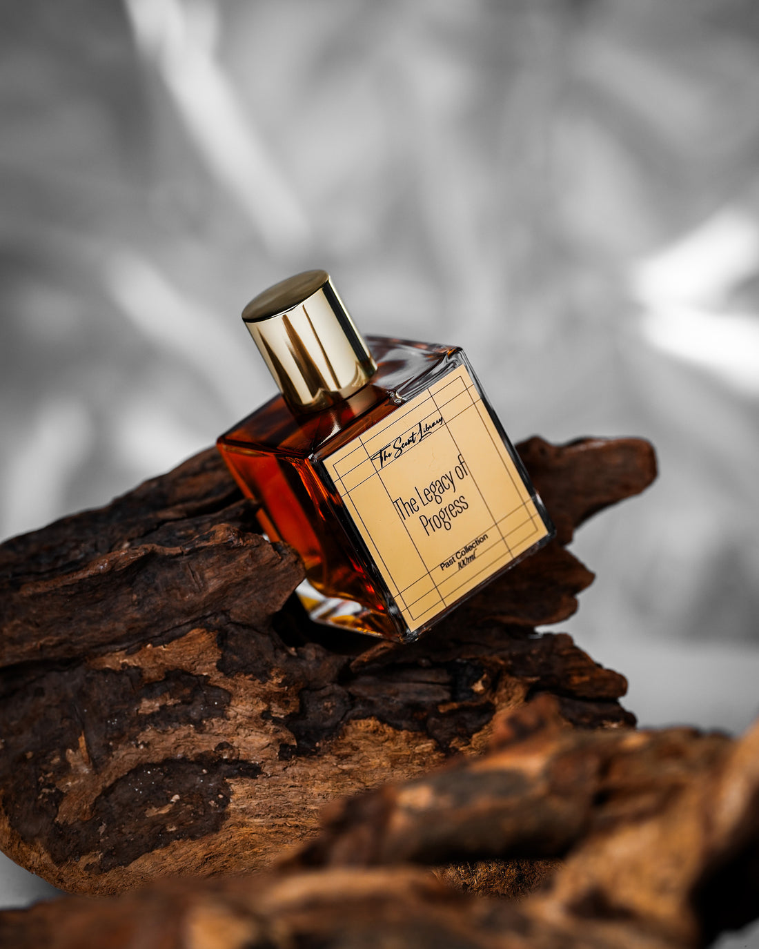 The Legacy of Progress perfume by The Scent Library, a clear gold-capped glass bottle on a wooden table in a lifestyle setting, Past Collection