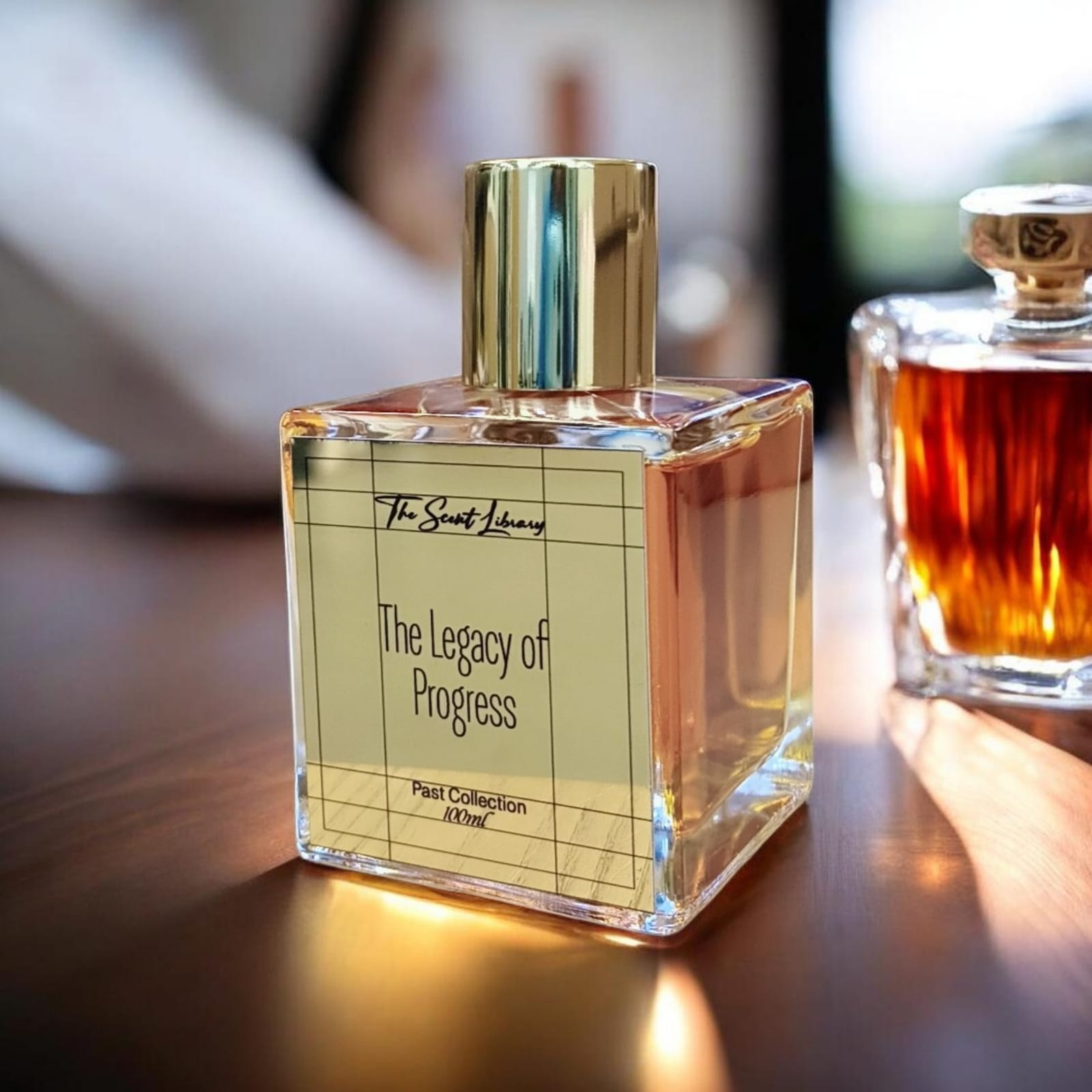 The Legacy of Progress perfume by The Scent Library, a clear gold-capped glass bottle on a wooden table in a lifestyle setting, Past Collection