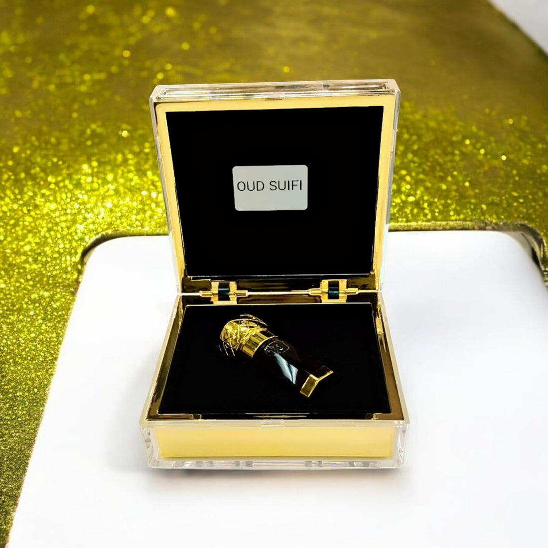 Oud Saufi Super by The Scent Library, an amber oud oil vial with an ornate gold cap displayed in an open gold-and-glass presentation box