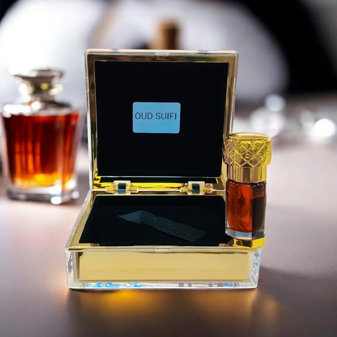 Oud Saufi Super by The Scent Library, an amber oud oil vial with an ornate gold cap displayed in an open gold-and-glass presentation box